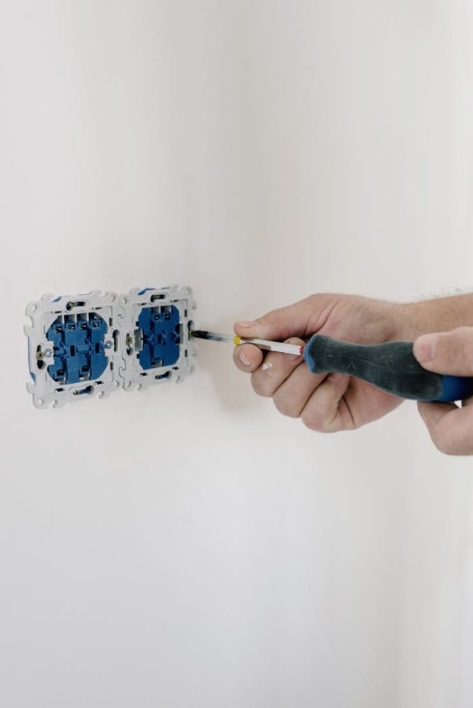 Crop faceless man using screwdriver for installation switches in apartment with light wall in daytime